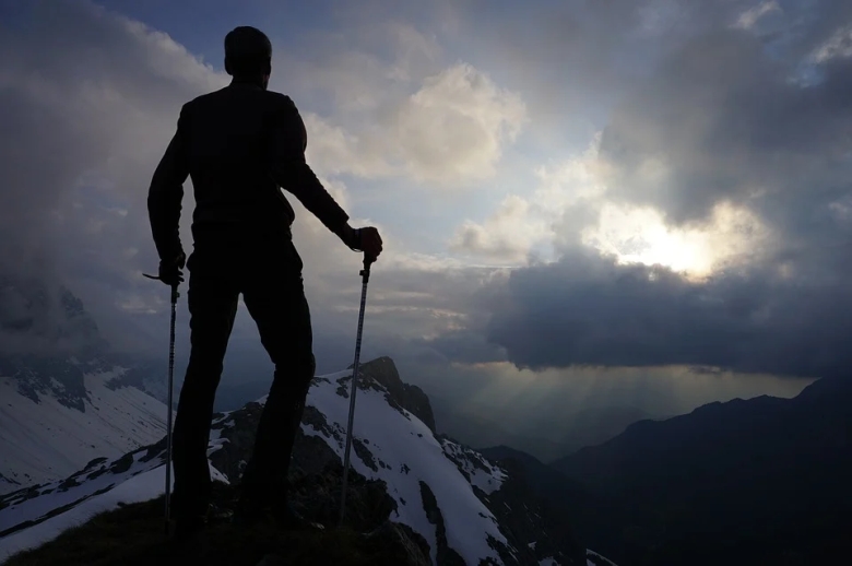 man standing on a mountain with two tactical walking sticks